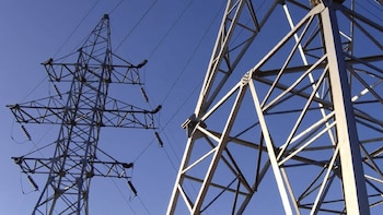 Dos torres de transmisión eléctrica de metal y líneas de alta tensión sobre un cielo azul