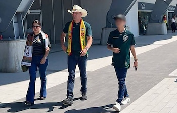 Edmand Lara, con sombrero vaquero blanco y bufanda boliviana, camina junto a Diana Romero y un joven con camisetas verdes y bufandas