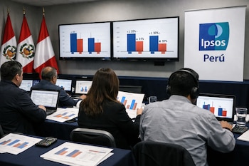 Vista trasera de personas analizando datos electorales en laptops y gráficos impresos en una sala de prensa con pantallas que muestran barras de resultados.