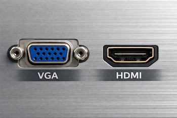 Primer plano de un panel de metal cepillado que muestra un puerto VGA azul a la izquierda y un puerto HDMI negro a la derecha, ambos etiquetados.