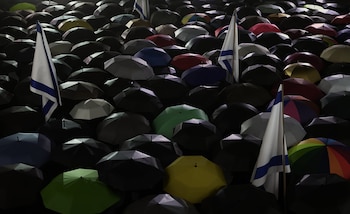 Vista aérea de numerosos paraguas abiertos, principalmente negros, con otros en colores verde, amarillo, rojo, azul, gris y multicolor. Varias banderas de Israel se alzan