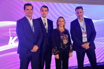 Grupo de cuatro profesionales, tres hombres y una mujer, de pie en un escenario iluminado con tonos morados y el logo de KPMG de fondo