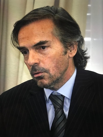 Primer plano del juez Gustavo Hornos con traje a rayas, camisa azul y corbata rayada. Mira hacia abajo con expresión seria