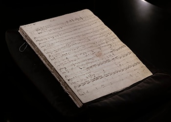 Un libro antiguo abierto muestra páginas con notación musical manuscrita, pentagramas y notas sobre un fondo negro, con encuadernación visible