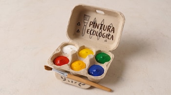 Caja de huevos abierta con seis compartimentos llenos de pinturas de colores, la frase Pintura ecológica en la tapa y un pincel.