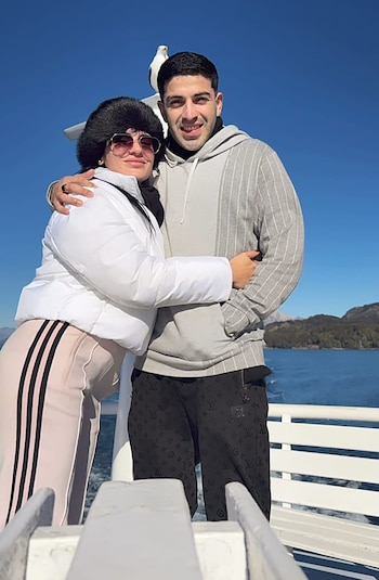 Pareja joven posando en una embarcación, con un cielo azul claro y montañas distantes. La mujer usa un gorro de piel negro y chaqueta blanca, el hombre un buzo gris