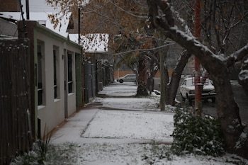 Una calle nevada con casas, árboles con ramas cubiertas de nieve y dos vehículos estacionados en el lado derecho de la vía