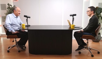 Dos hombres sentados frente a una mesa oscura con micrófonos. El hombre de la izquierda (Adam Fox) usa camisa azul; el de la derecha, camisa oscura