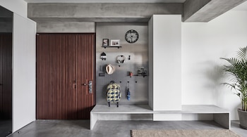 Entrada de una vivienda con una puerta de madera, un panel de almacenamiento perforado, un reloj, fotos, auriculares, sombrero, mochila, paraguas, banco y una planta.