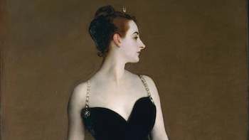 Retrato de una mujer de perfil con cabello oscuro recogido, vestida con un top negro de tirantes dorados, sobre un fondo marrón liso