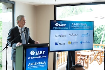 Un hombre de traje habla desde un atril con micrófono al lado de una pantalla informativa sobre la 47 Convención Anual del IAEF