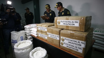 Agentes de la Policía Nacional del Perú junto a cajas etiquetadas como incautación, sacos de polvo blanco con la palabra yeso y un camarógrafo con cámara.