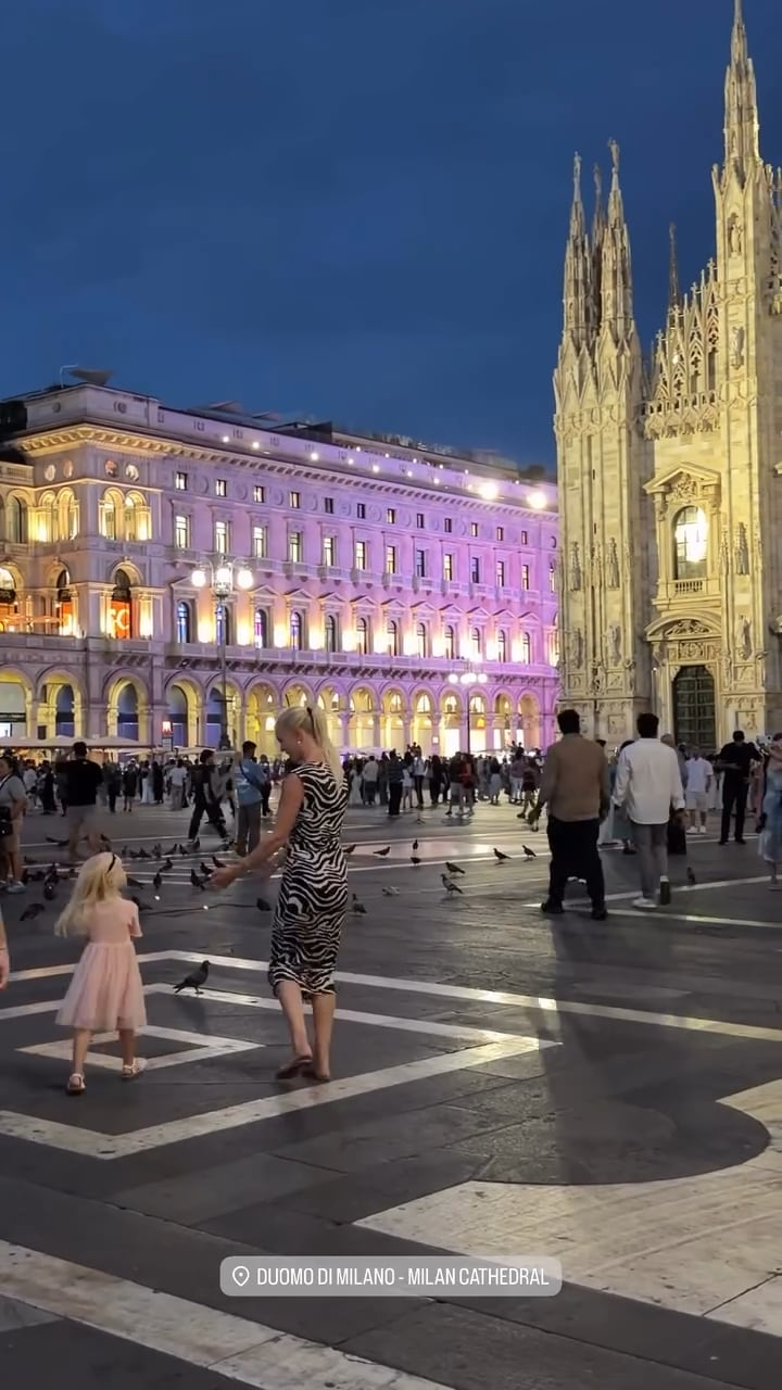 Daniela Christiansson interactúa con su hija en la plaza del Duomo de Milán ante la fachada iluminada de la catedral.