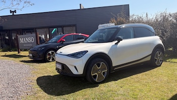 Un automóvil eléctrico blanco y otro negro con techo rojo estacionados en el césped frente a un restaurante