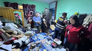Agentes policiales y fiscales revisan una habitación con dinero, armas, teléfonos y pasaportes extendidos sobre la cama