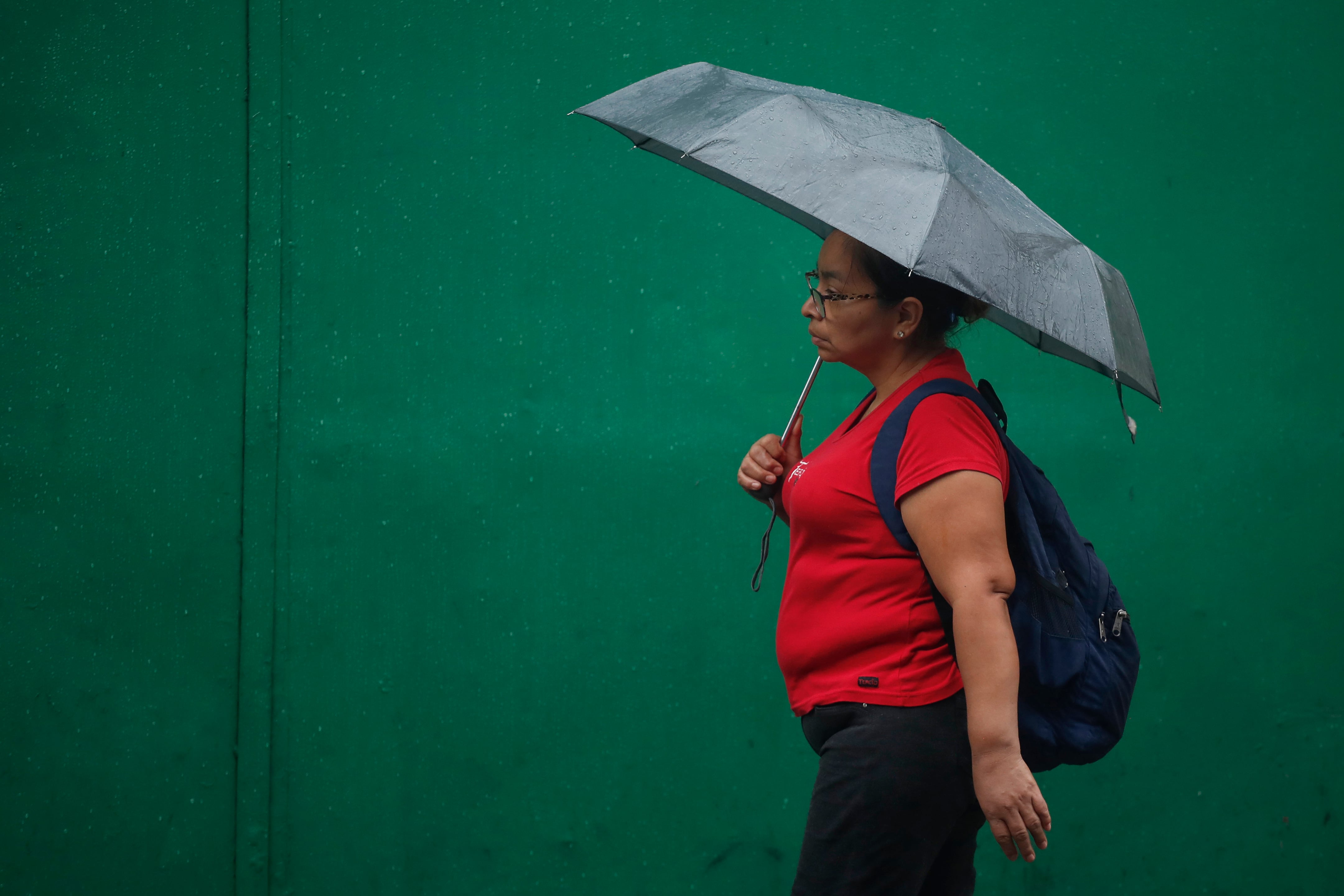 Una mujer se protege de la lluvia en el centro de San Salvador (El Salvador). EFE/Rodrigo Sura
