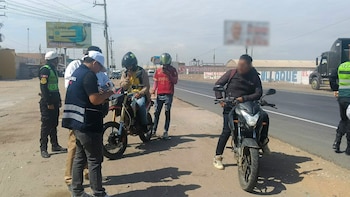 Personal con chaleco de Migraciones y policías inspeccionan a conductores en motocicletas al costado de una carretera asfaltada