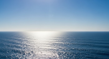 Vista panorámica de un océano azul bajo un cielo despejado, con el sol reflejándose intensamente sobre la superficie del agua.