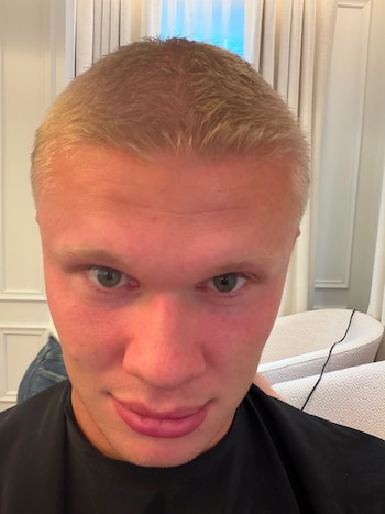 Primer plano del futbolista Erling Haaland con el cabello rubio rapado y una peinador negro frente a sillones blancos