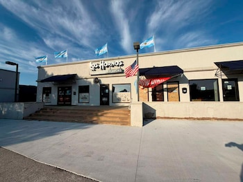 Edificio del Restaurante Los Hornos con banderas argentinas en el tejado y una bandera estadounidense en la fachada. Hay escaleras que conducen a la entrada principal con toldos azules