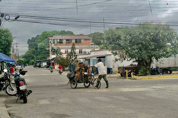 Un hombre empuja un triciclo de carga en una calle asfaltada con motocicletas aparcadas, edificios y tendido eléctrico