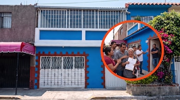 Fachada de casa azul con portón blanco y un detalle circular que incluye a personas y una mujer con documentos.