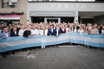 Gran grupo de personas, incluyendo a Axel Kicillof y Ricardo Quintela, sosteniendo una bandera argentina frente al edificio de la Federación Argentina de Municipios