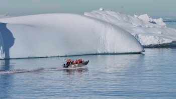 Bote con motor navega en aguas azules junto a grandes icebergs. Varias personas con chalecos salvavidas anaranjados ocupan la embarcación