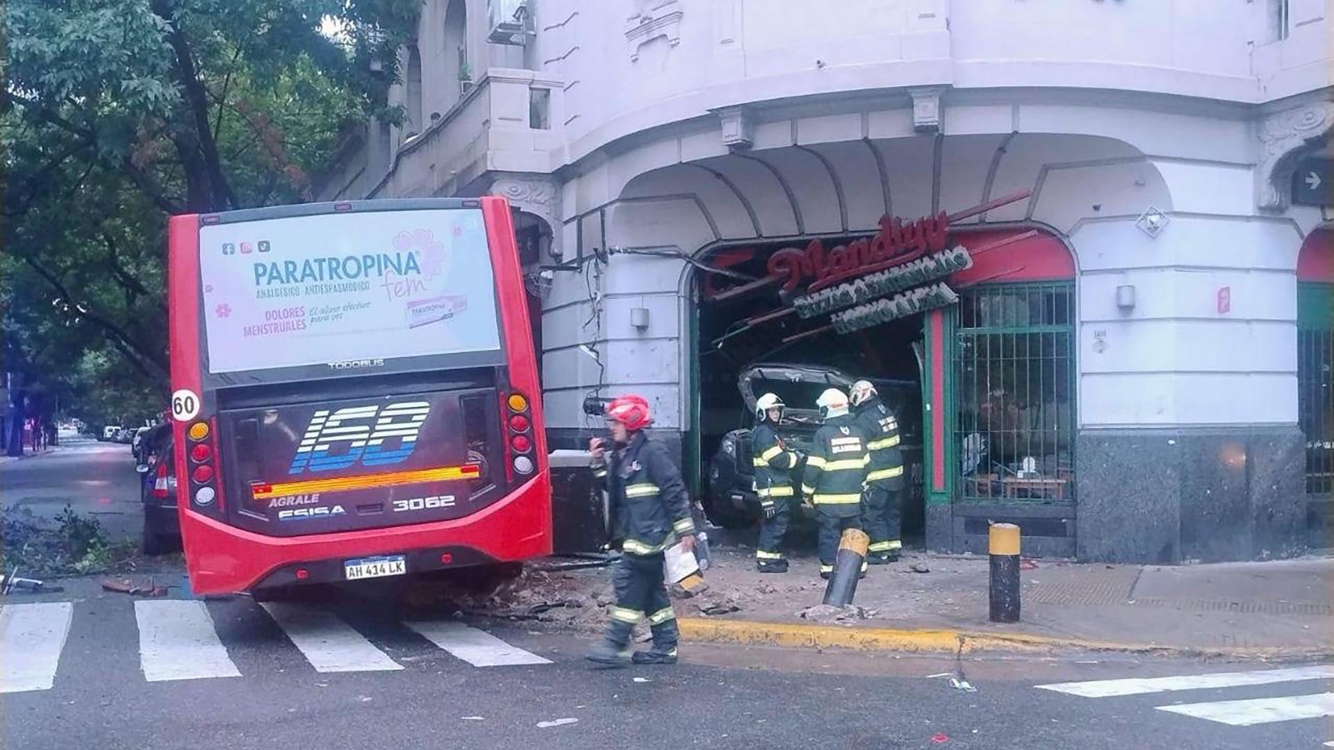 Un colectivo y un patrullero colisionaron, resultando en que ambos vehículos se empotraran contra la fachada de un comercio, mientras equipos de emergencia trabajan en el lugar.