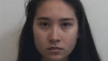 Primer plano de una mujer con cabello oscuro y liso, mirando fijamente a la cámara con una expresión seria sobre un fondo claro y liso