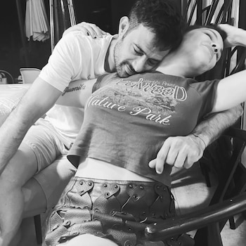 Imagen monocromática de un hombre barbudo abrazando a una persona con una camiseta y una falda de cuero con forma de corazón
