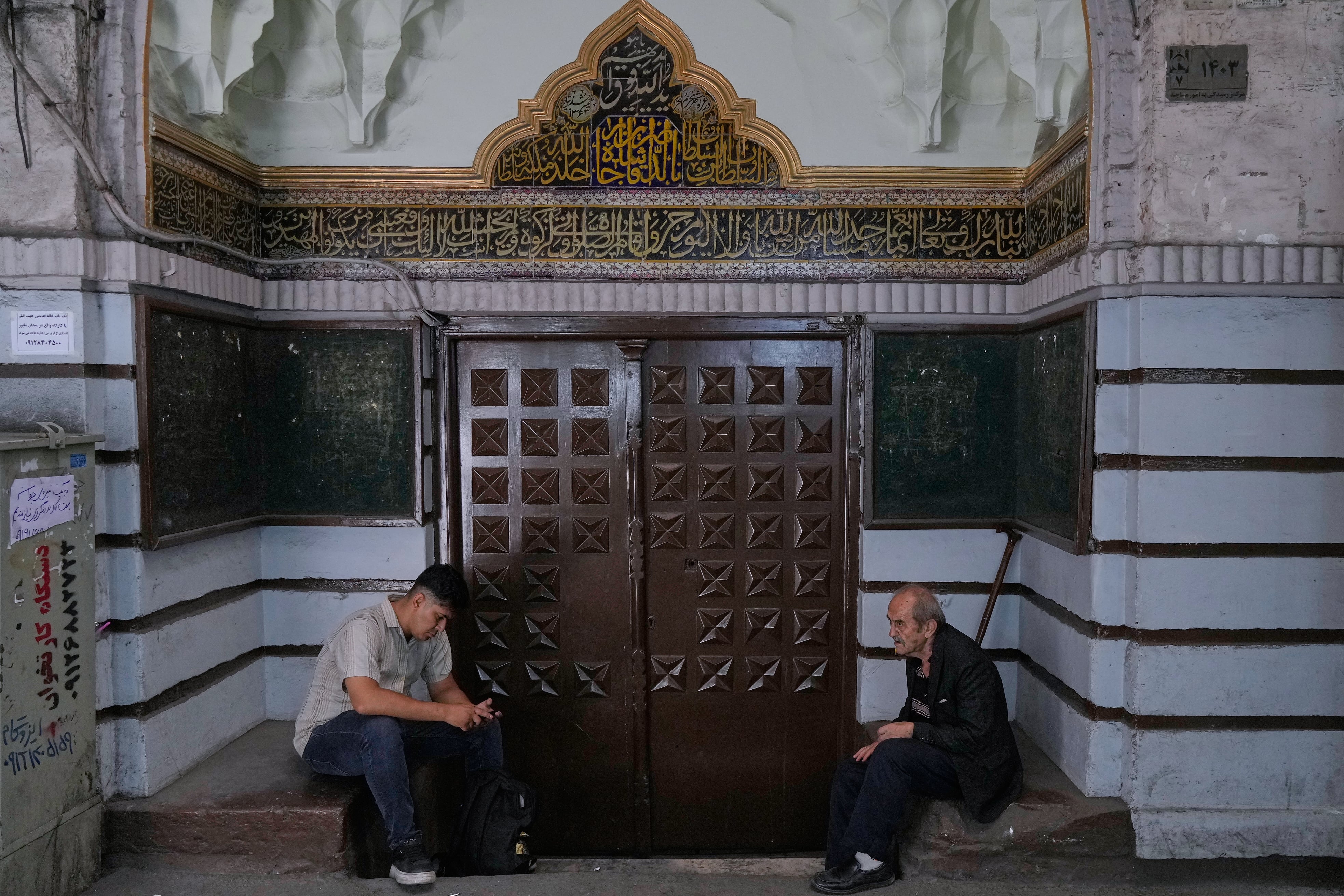Hombres descansan en la entrada de una mezquita del histórico Gran Bazar de Teherán, el lunes 1 de junio de 2026. La presión económica ya desencadenó protestas en enero que dejaron más de 7.000 muertos, según estimaciones de activistas. (AP Photo/Vahid Salemi)