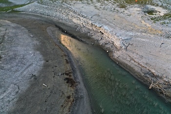 Vista aérea de un paisaje árido con un río angosto y poco profundo, rodeado de tierra agrietada y seca. Se observan formaciones rocosas y vegetación muerta