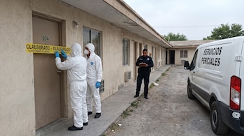 Dos peritos instalan cinta amarilla "CLAUSURADO" en la puerta de la habitación 104 de un motel. Un oficial de policía y una camioneta de Servicios Periciales están cerca.