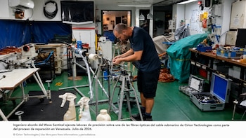 Un ingeniero manipula fibras ópticas en una sala de trabajo a bordo de un buque, rodeado de herramientas, maquinaria, cables y cajas