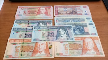 Vista superior de varios billetes de Quetzal guatemaltecos de 10, 20 y 50 denominaciones, ordenados y parcialmente superpuestos sobre una mesa de madera.