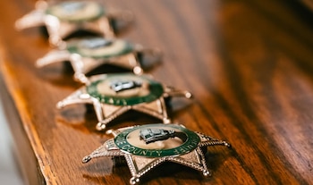 Cuatro insignias de sheriff en forma de estrella de color dorado con el centro verde y texto "Riverside County Sheriff" sobre una superficie de madera
