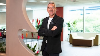 Christian Coone, hombre de cabello gris y traje oscuro, sonríe a cámara con los brazos cruzados dentro de una oficina con plantas y ventanas