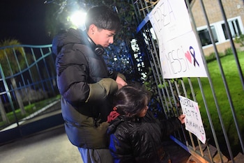 Un hombre joven y una niña colocan dos carteles escritos a mano en una reja metálica por la noche