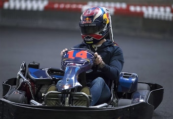 Un piloto con casco protector conduce un kart con el número catorce en una pista rodeada por barreras de protección
