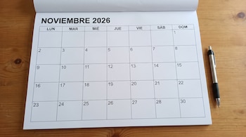 Un calendario en papel con los días de noviembre de 2026 sobre una mesa de madera clara al lado de un bolígrafo plateado.