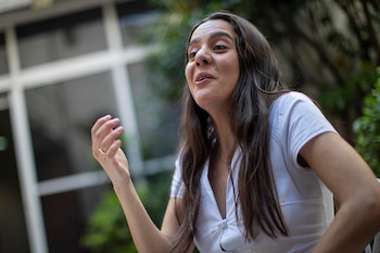 Valeria Castro, de cabello oscuro, viste una camisa blanca y tiene la boca ligeramente abierta, con su mano derecha levantada y un anillo visible