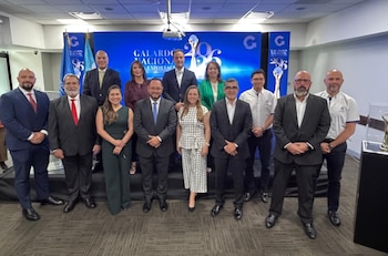 Once personas vestidas con trajes formales posan de pie delante de una pantalla azul con el logotipo del Galardón Nacional a la Exportación