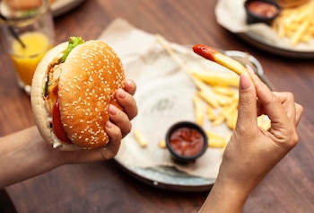 Una mujer comiendo una hamburguesa con patatas (Magnific)