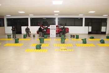 Oficiales de Gendarmería Nacional junto a un perro en una sala, con una camioneta roja y numerosas tabletas amarillas y bolsas verdes de estupefacientes en el suelo