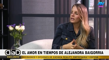 Alejandra Baigorria sentada en un sofá en un set de televisión con un ramo de flores y el logo del programa Día D