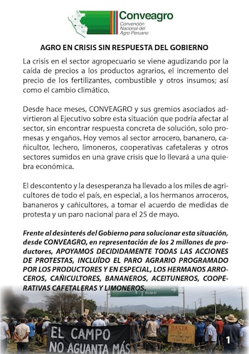 Vista de manifestantes en una carretera bloqueada, portando pancartas negras con letras blancas y una pequeña pancarta amarilla. Se observa humo y señalización de carretera