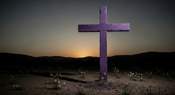 Cruz de madera morada en un campo seco al atardecer, con pequeñas flores blancas y montañas al fondo bajo un cielo degradado.