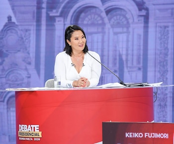 Keiko Fujimori, vestida de blanco, sentada en un podio rojo con micrófono. El podio dice "DEBATE PRESIDENCIAL" y hay un cartel "KEIKO FUJIMORI"