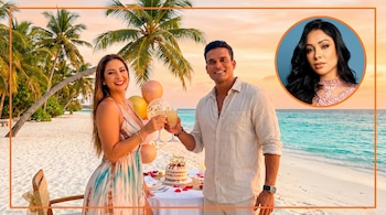 Pareja brinda en playa tropical al atardecer con palmeras, arena blanca, mar turquesa y pastel de cumpleaños. Inset circular de Pamela Franco arriba a la derecha.